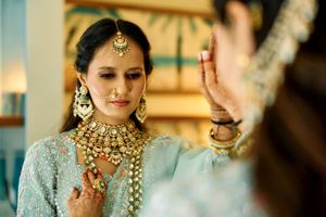 Indian bride in light blue outfit admiring ornate gold kundan jewelry set in mirror reflection.