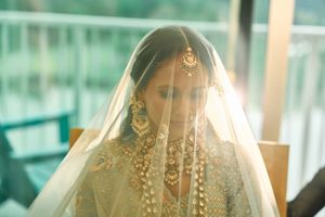 Indian bride in white veil and gold kundan jewelry with maang tikka and chandelier earrings at wedding.