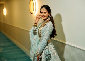 Beautiful Indian bride in light blue lehenga with gold jewelry smiling at a wedding celebration.