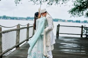 Indian bride and groom sharing a kiss on a wooden dock by the lake in the rain.