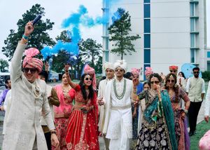 Colorful Indian wedding baraat procession with guests in vibrant attire and blue smoke celebration outdoors.