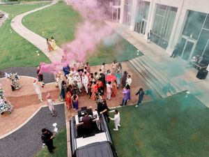 Aerial view of Indian wedding guests celebrating with colorful pink and blue smoke bombs outside.