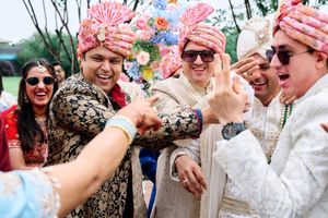 Groom in white sherwani celebrating with groomsmen in colorful turbans during Indian wedding baraat.