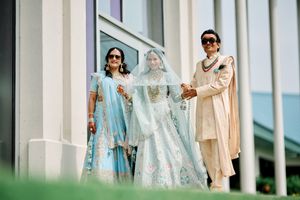 Indian bride in light blue lehenga walks with family during traditional wedding ceremony outdoors.