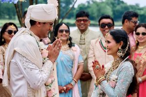 Indian bride and groom greeting with namaste gesture at outdoor wedding ceremony.