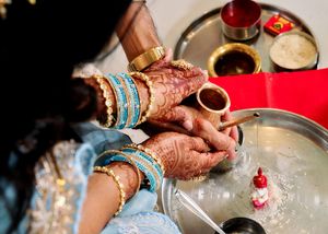 Close-up of bride's henna-adorned hands with blue bangles during traditional Indian wedding ritual ceremony.
