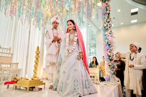 Indian bride and groom walking together at ceremony under pastel floral ceiling decorations.