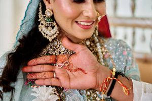 Indian bride smiles showing mehndi infinity symbol on palm wearing ornate kundan jewelry and blue dupatta.