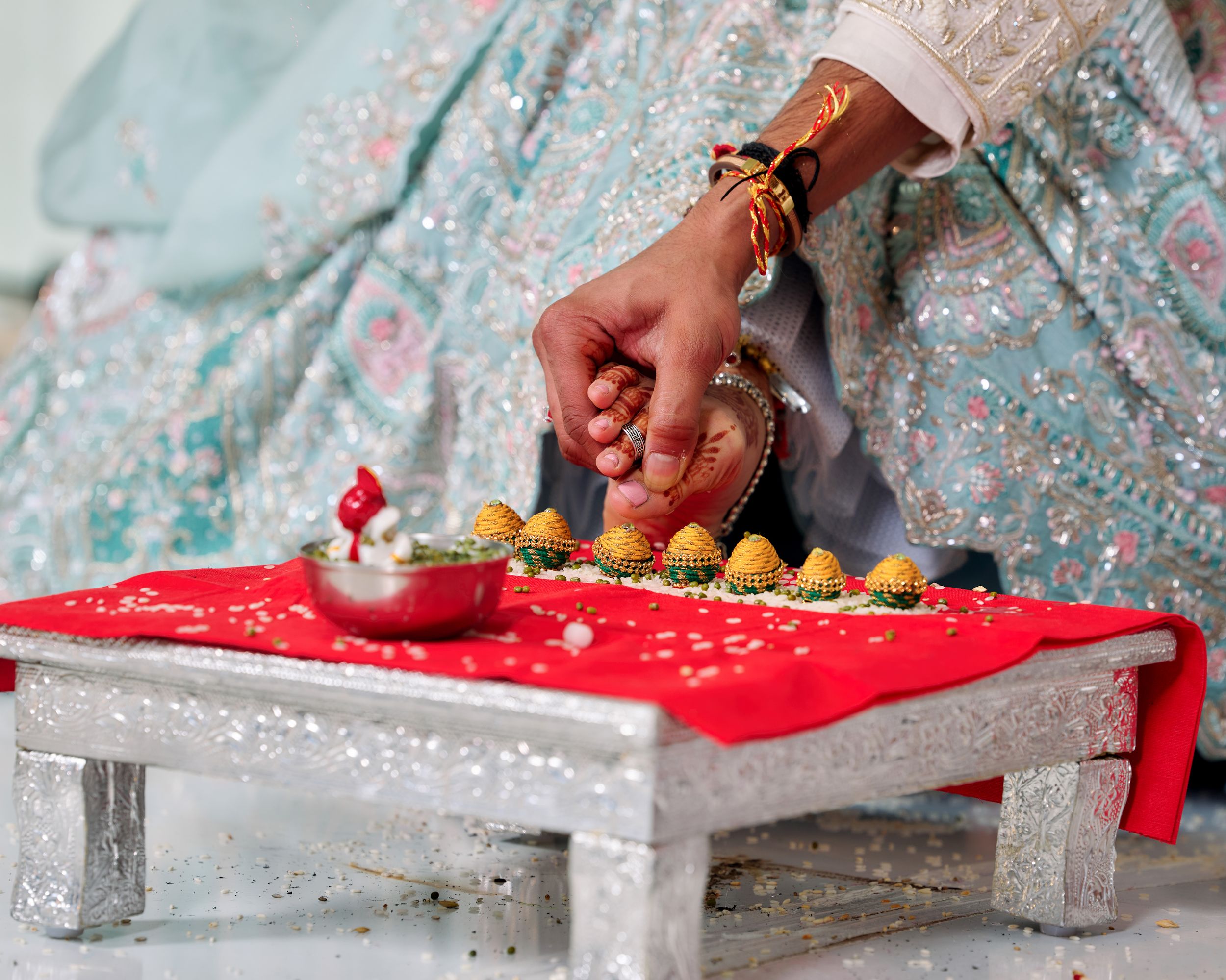 Close-up of hands performing Indian wedding ritual with sweets and diya on red cloth during traditional ceremony.