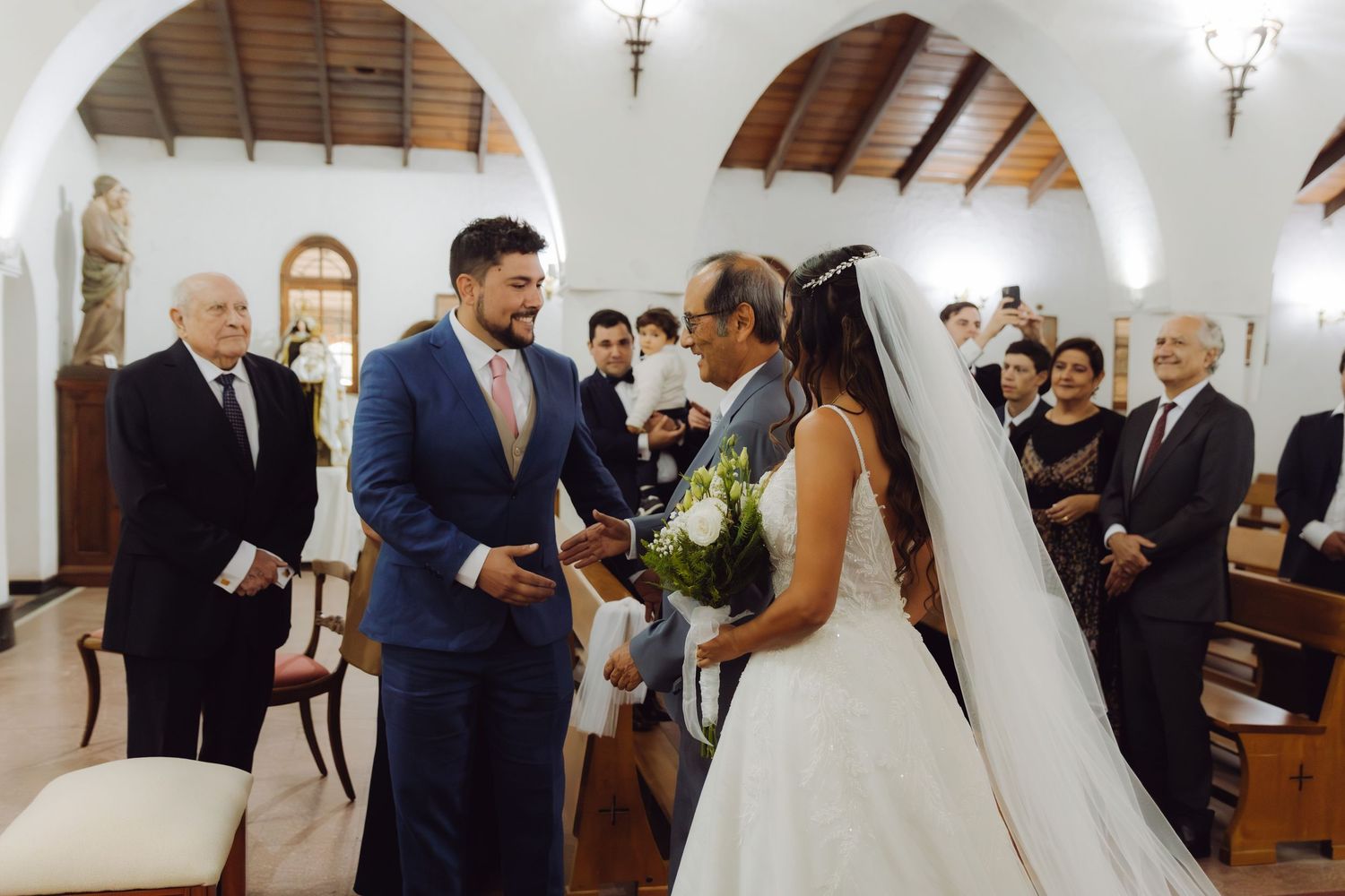 Groom in blue suit meets bride in white gown at church altar during wedding ceremony.