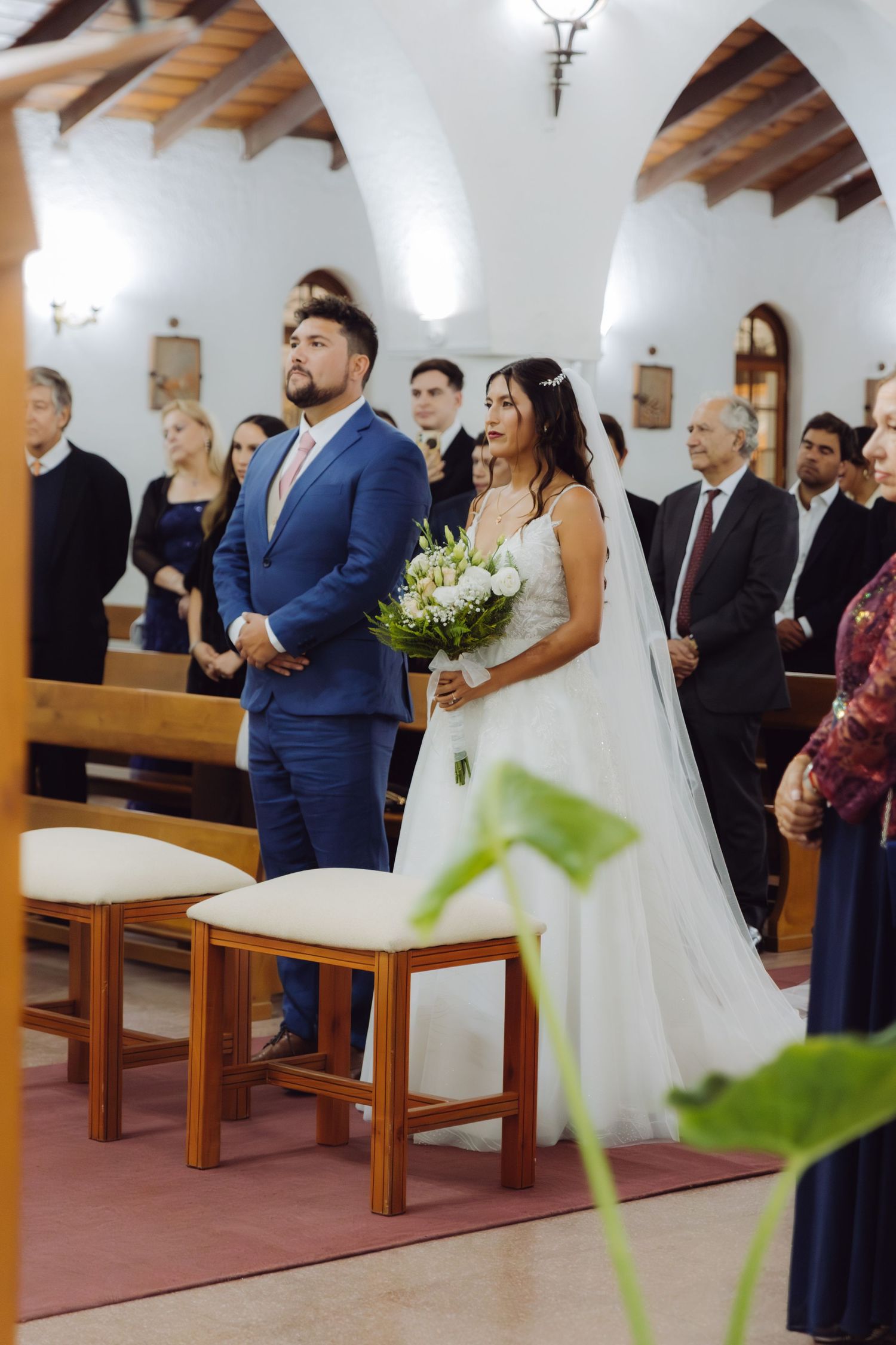 Bride and groom stand together at church altar holding white flower bouquet during ceremony.