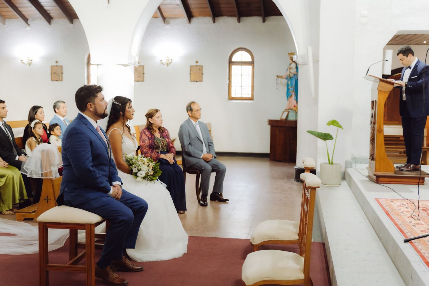 Bride and groom sit at church altar listening to officiant during wedding ceremony.