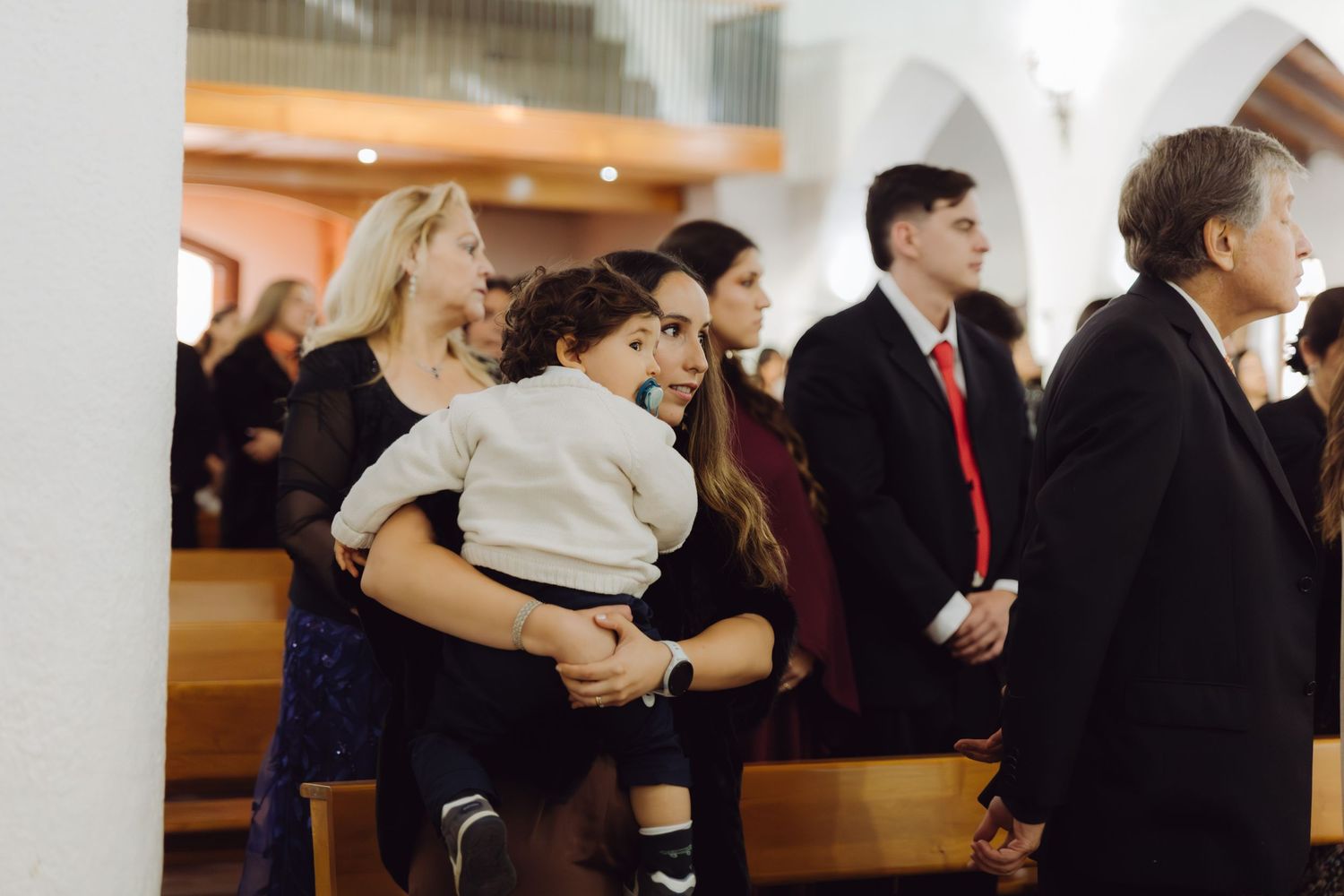 Wedding guest holds young child while standing in church during wedding ceremony.