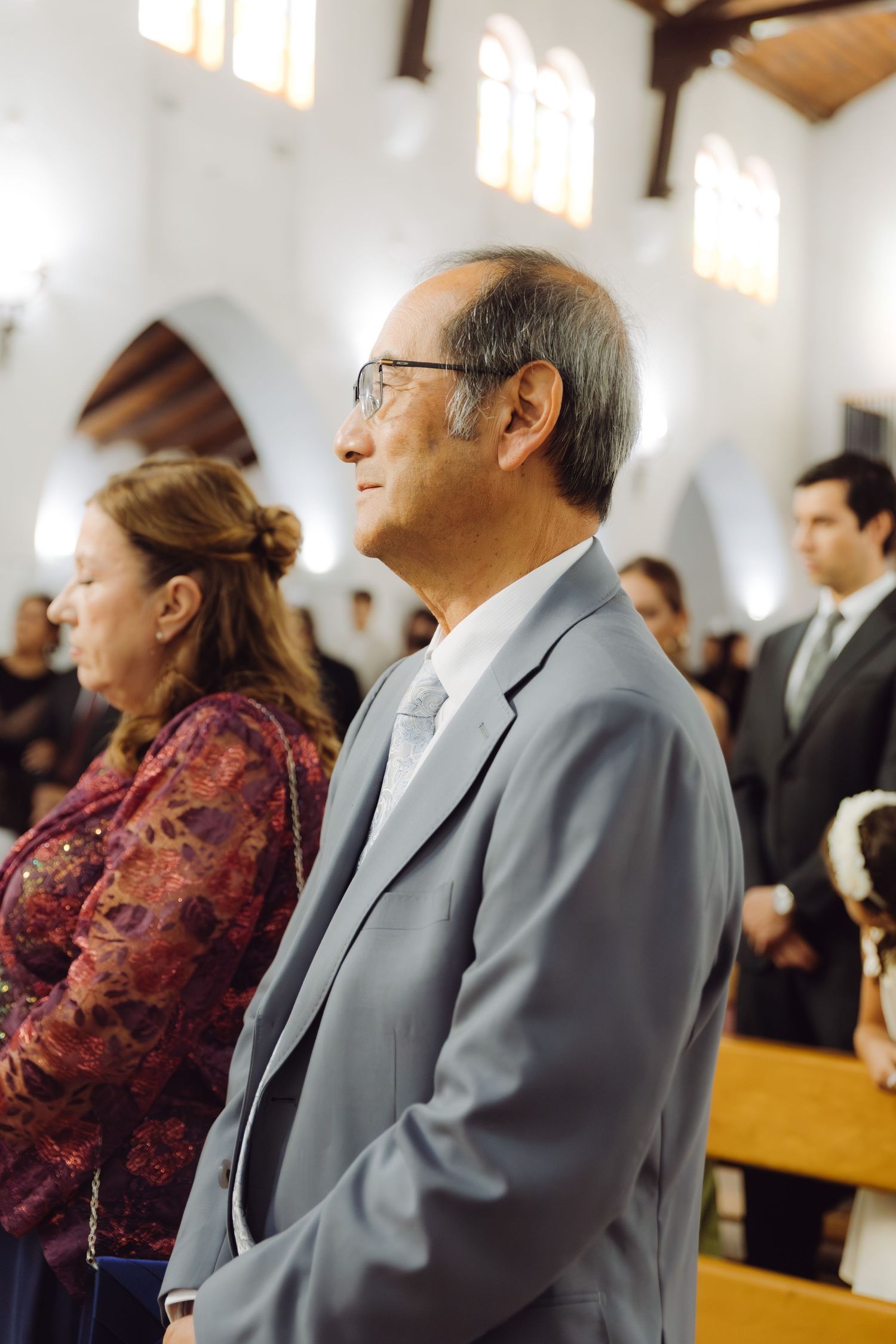 Elderly man in gray suit smiling during a church wedding ceremony.