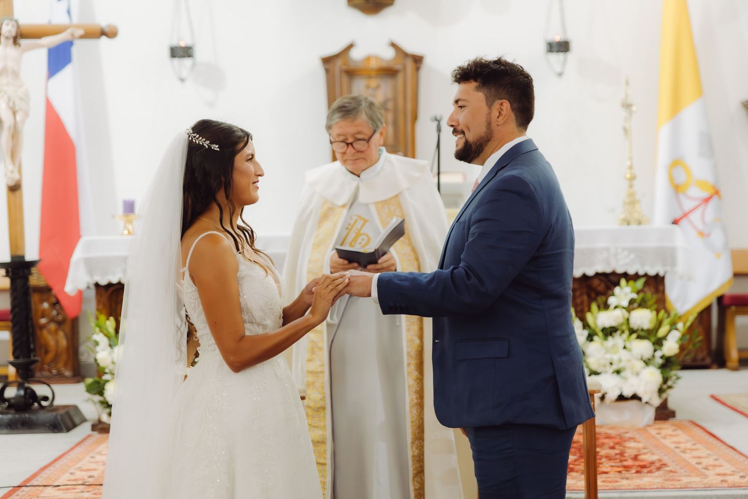Bride places wedding ring on grooms finger during a Catholic church ceremony.