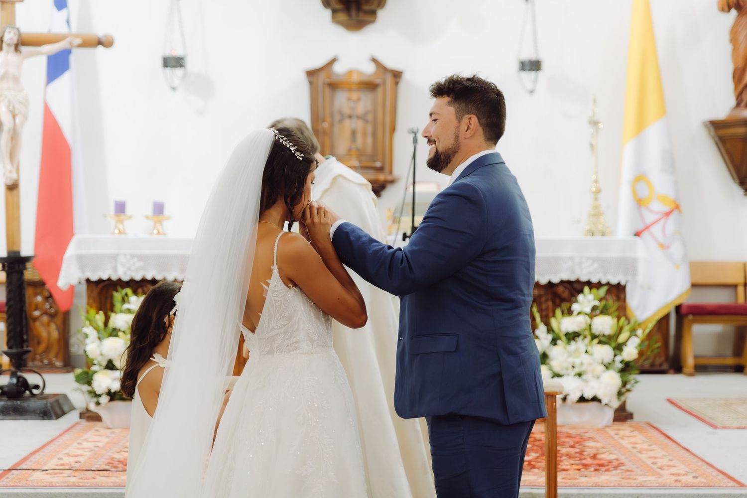 Groom tenderly adjusts brides veil at the altar during their church wedding ceremony.