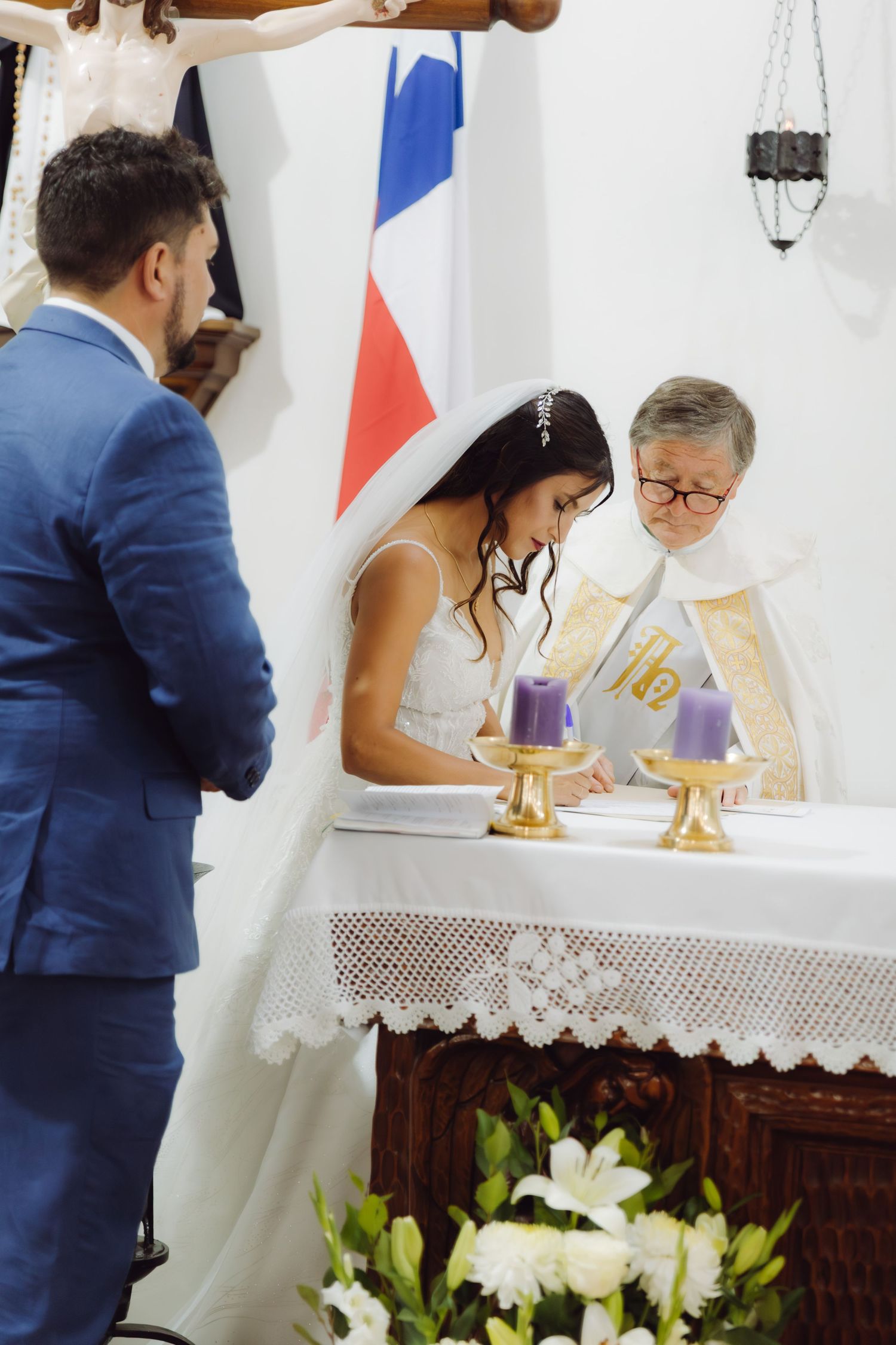 Bride signs wedding register at the altar with priest during a Catholic ceremony.