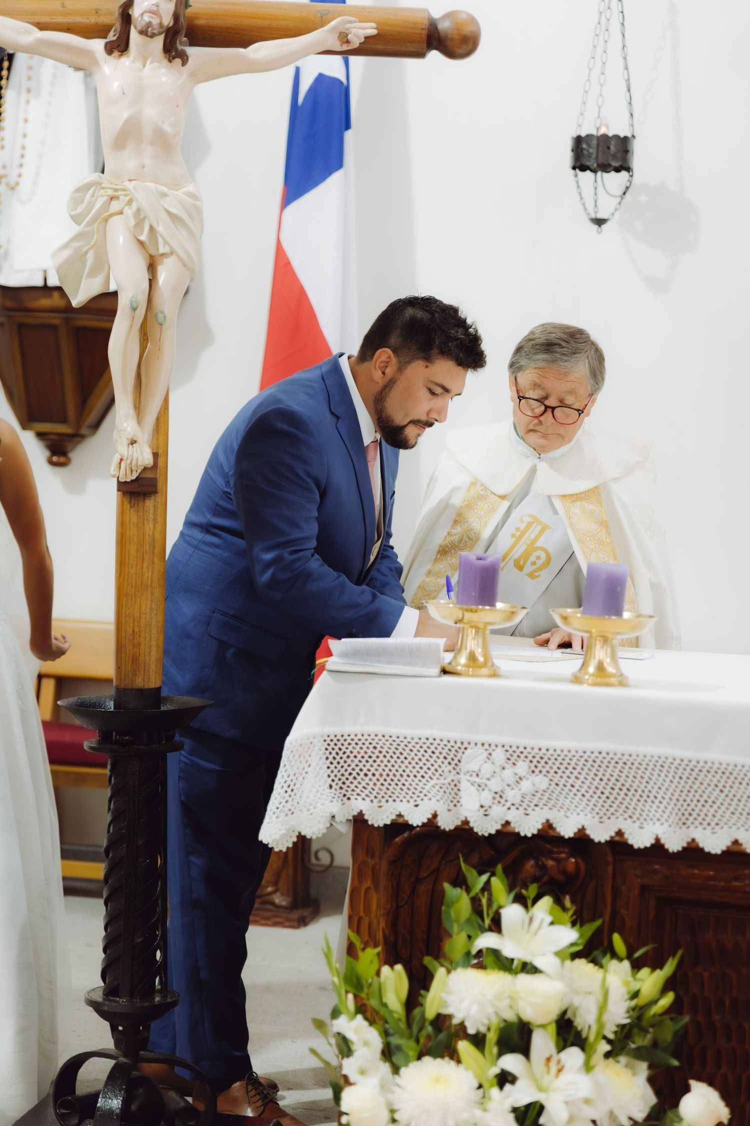 Groom signs wedding register at the altar with priest during a Catholic ceremony.