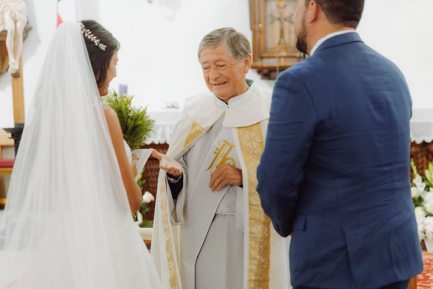 Catholic priest reads from book during wedding ceremony with bride and groom at the altar.