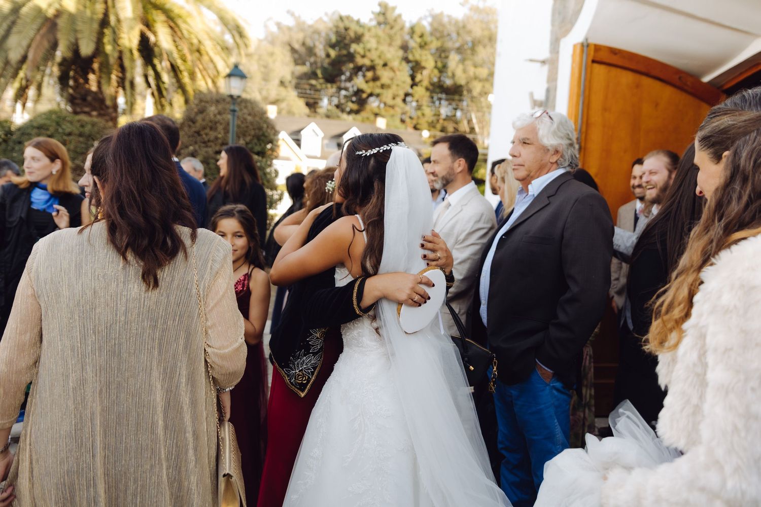 Bride in white dress and veil mingles with wedding guests outside church doors after ceremony.