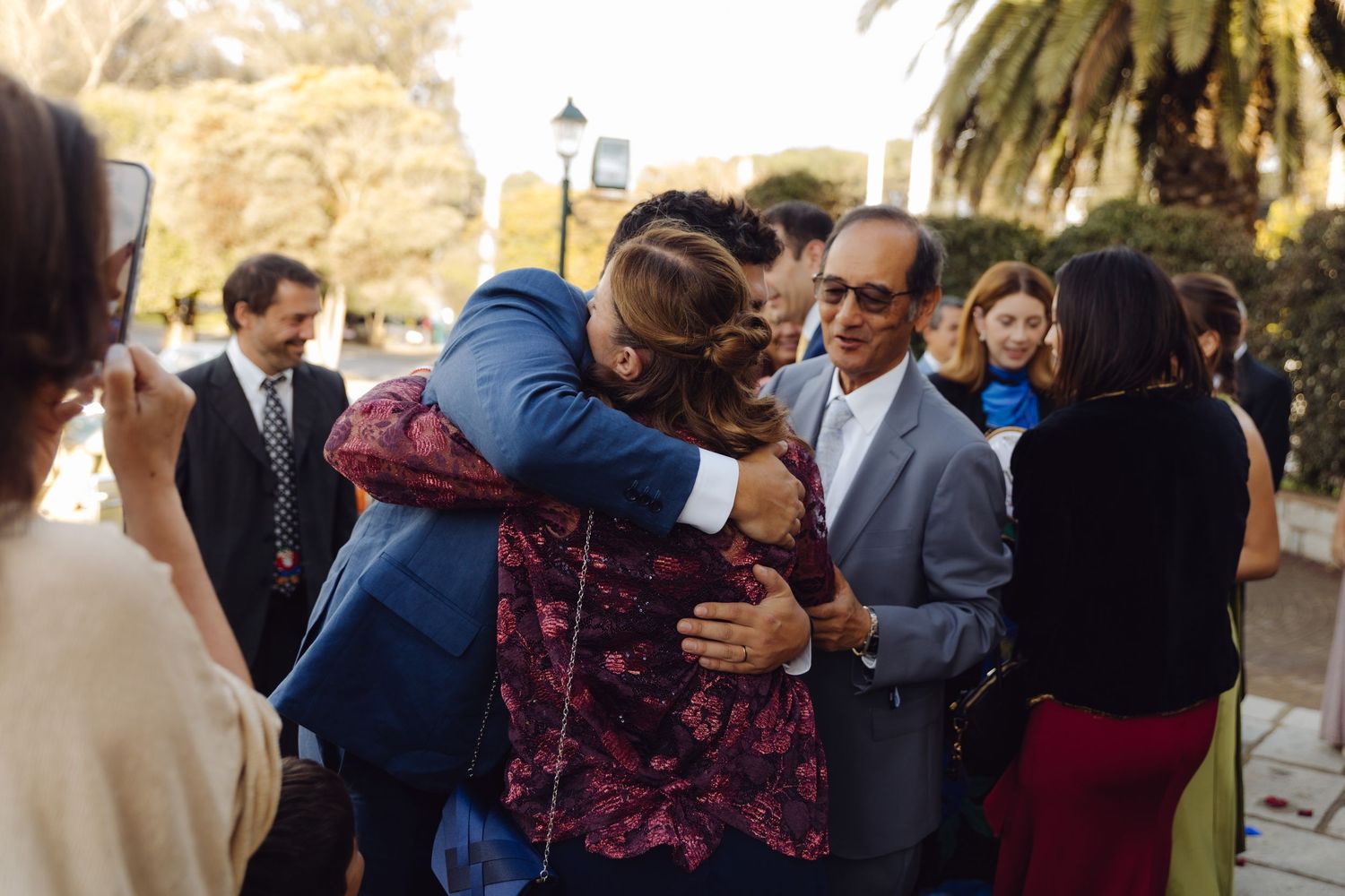 Guests hugging and greeting each other at an outdoor wedding reception near palm trees.