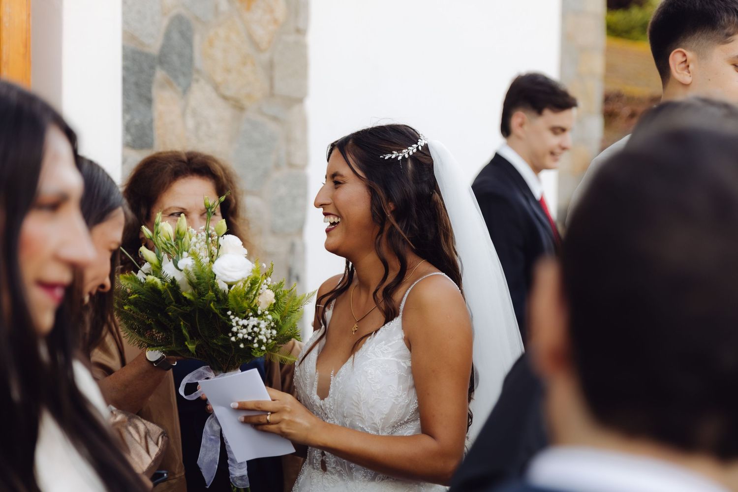 Smiling bride in white lace gown holding a bouquet of white flowers at her wedding.