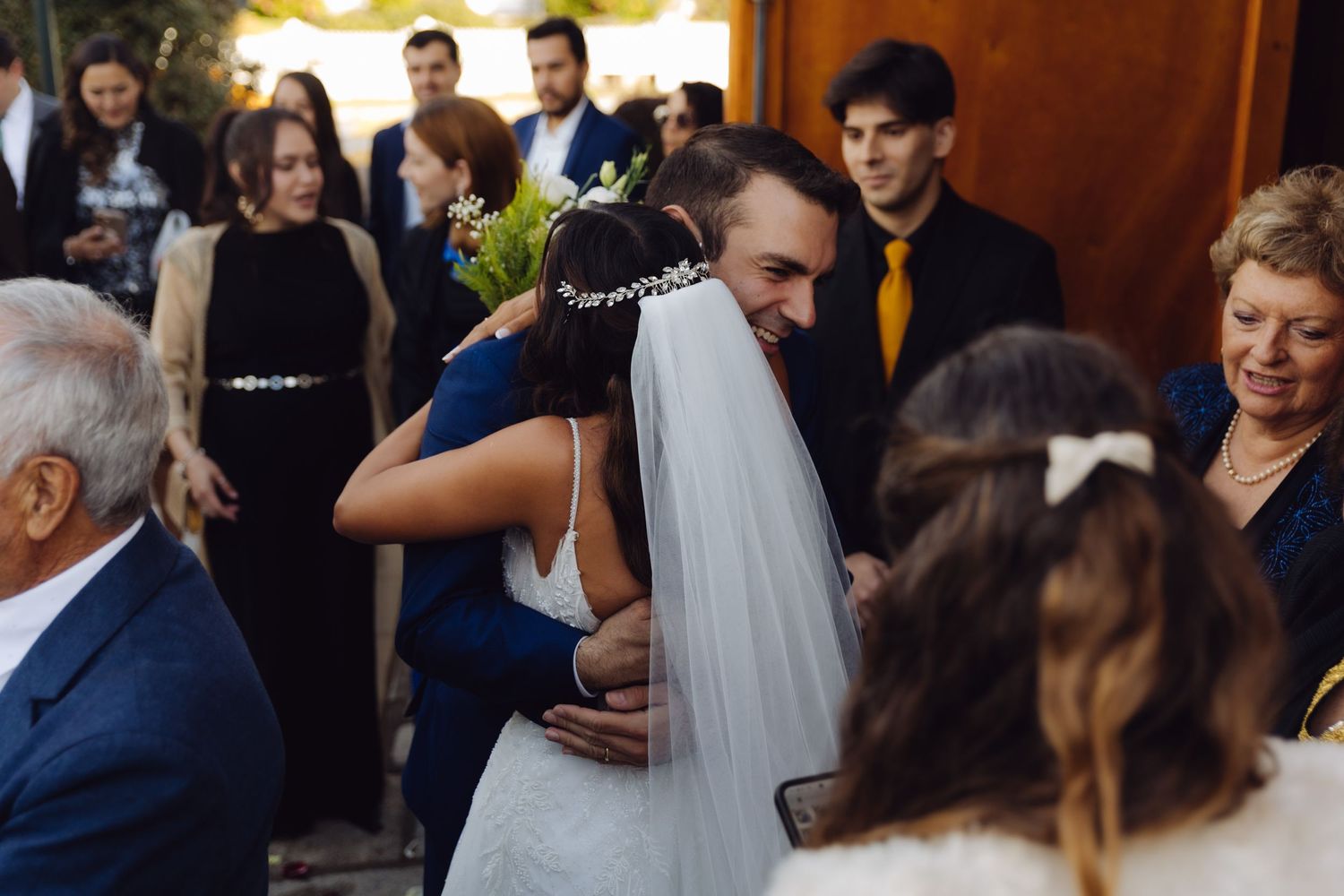 Groom in blue suit embracing bride in white wedding dress during outdoor ceremony.