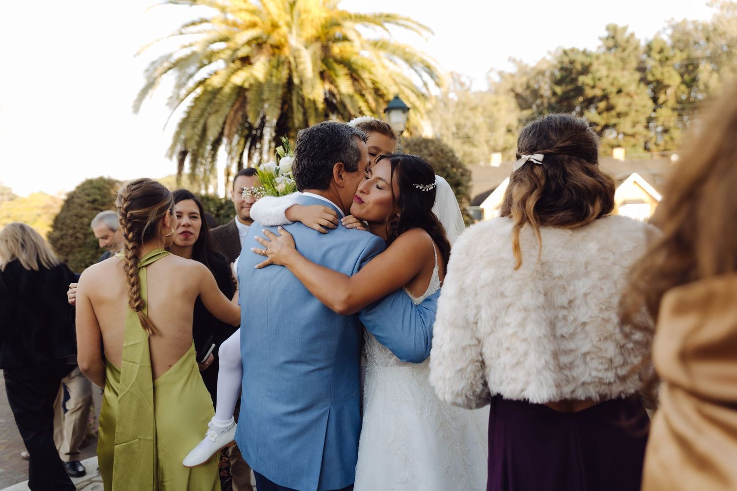 Bride in white gown embracing a guest in a blue suit at an outdoor wedding reception.