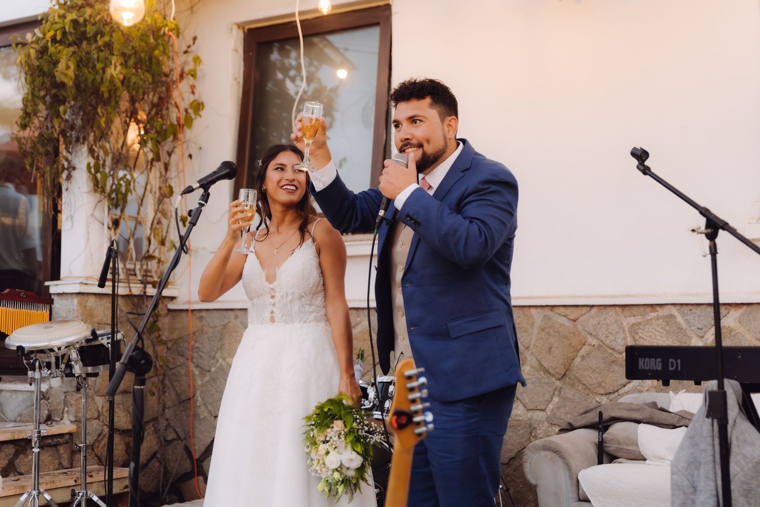 Bride and groom raising glasses in a toast at their outdoor wedding reception with live band.
