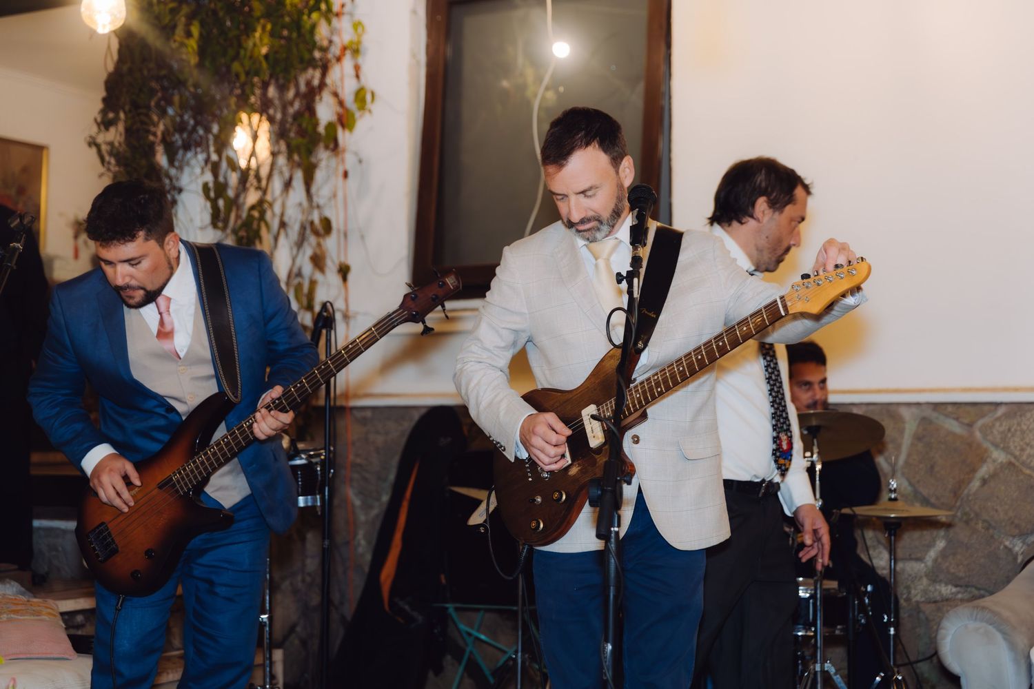 Live band with three musicians playing electric guitars at an elegant indoor wedding reception.