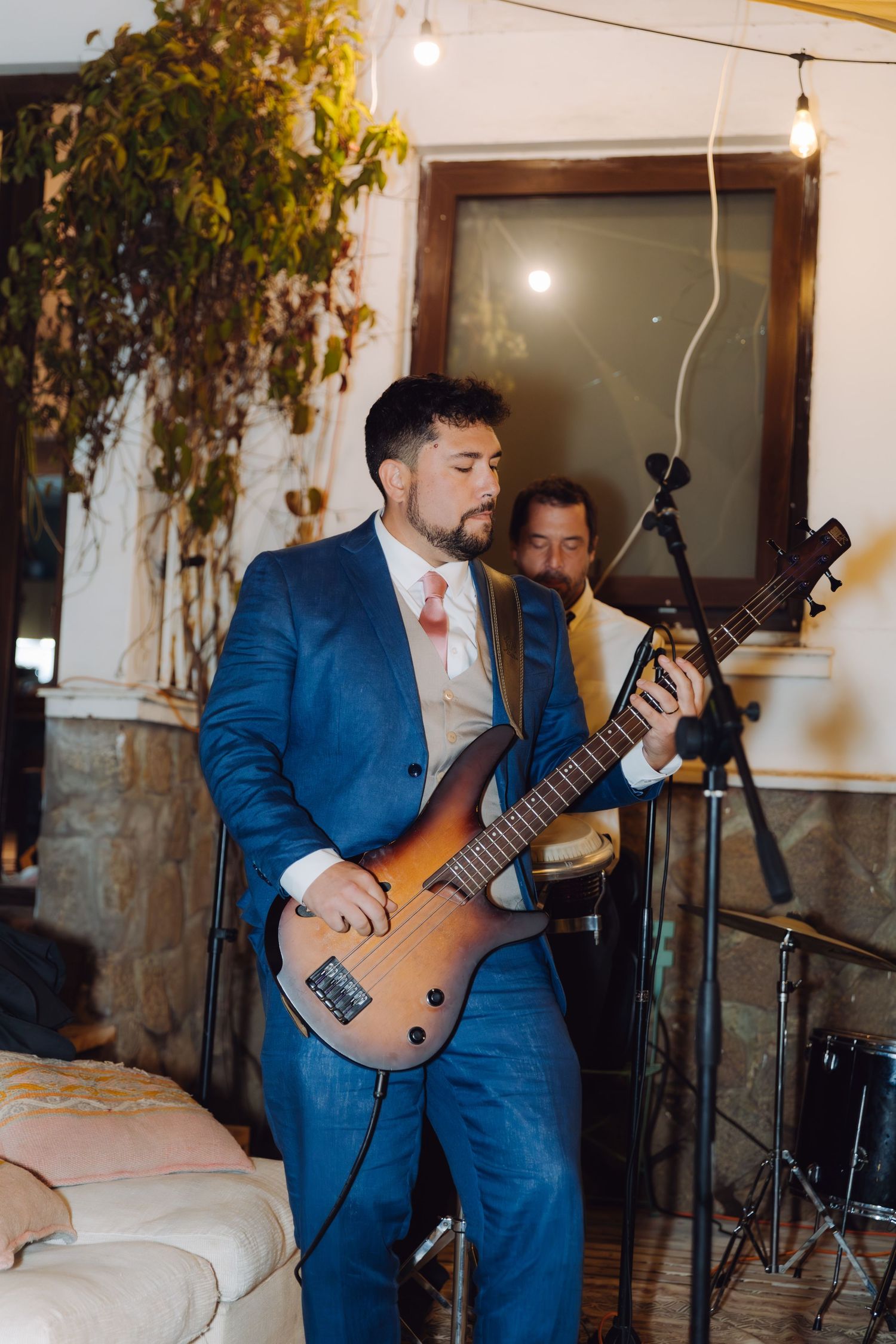 Groom in blue suit playing bass guitar during live band performance at wedding reception.