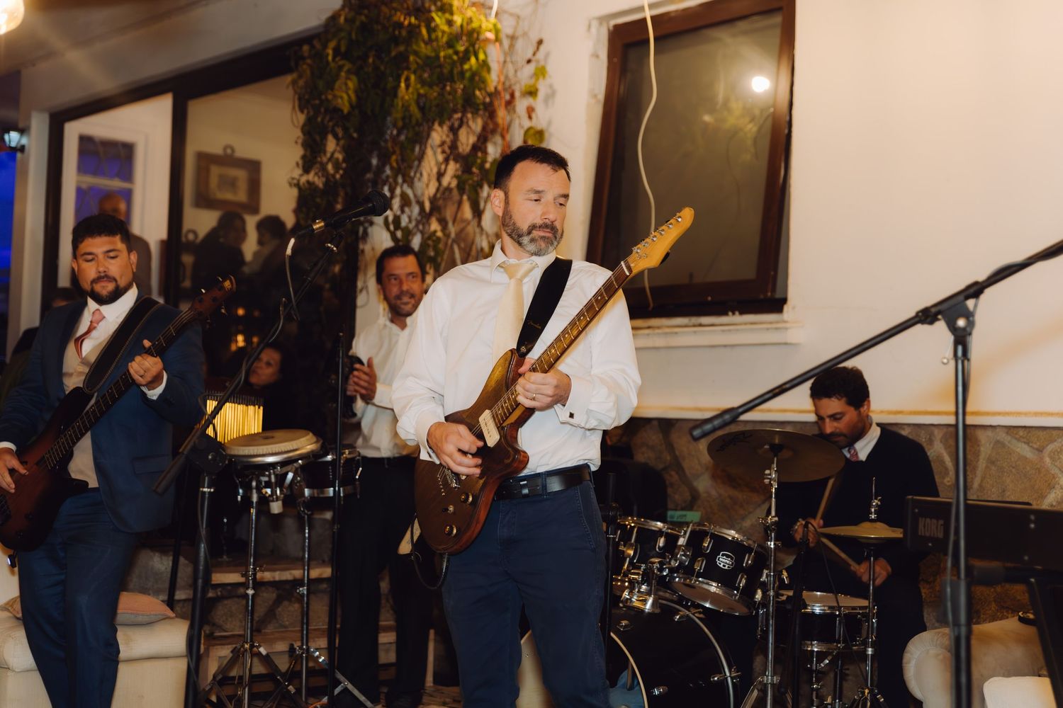 Live wedding band performing energetically indoors with guitarist in white shirt leading the group.