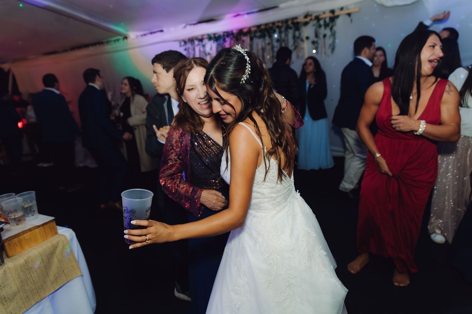 Bride hugs guest while dancing at lively wedding reception party.