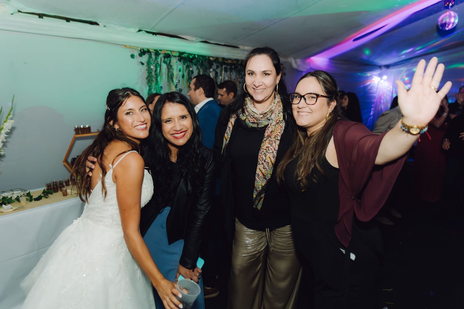 Bride poses with three smiling female guests at wedding reception celebration.