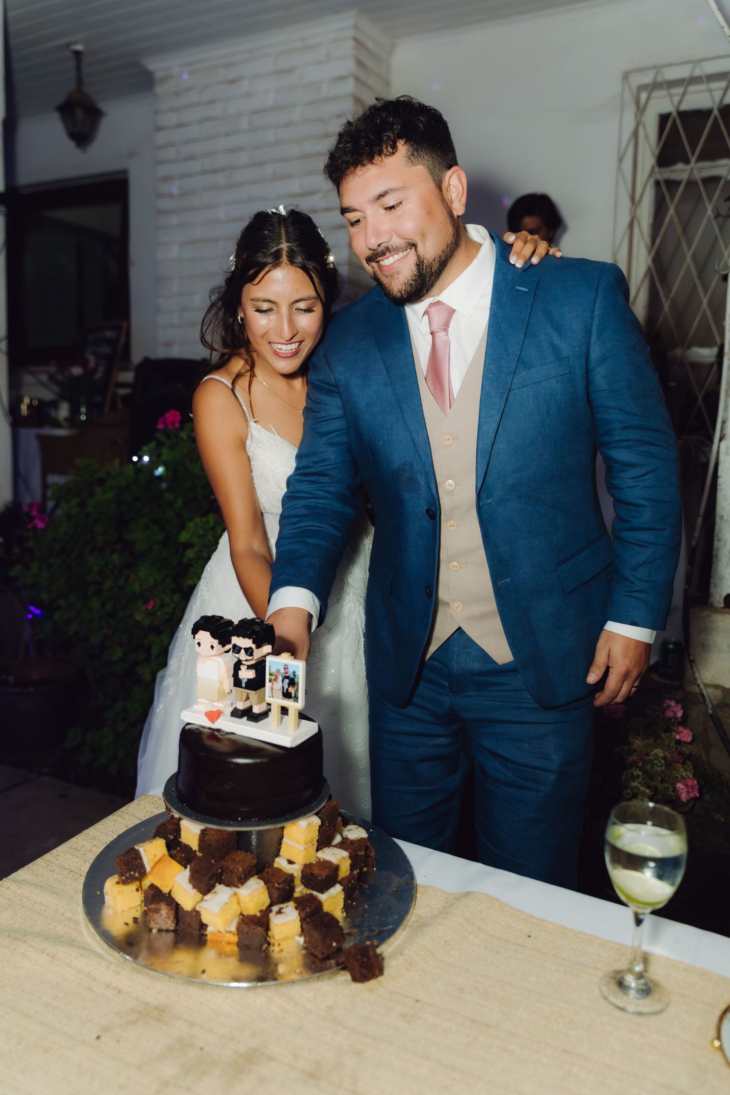Smiling bride and groom in blue suit cut chocolate wedding cake together.