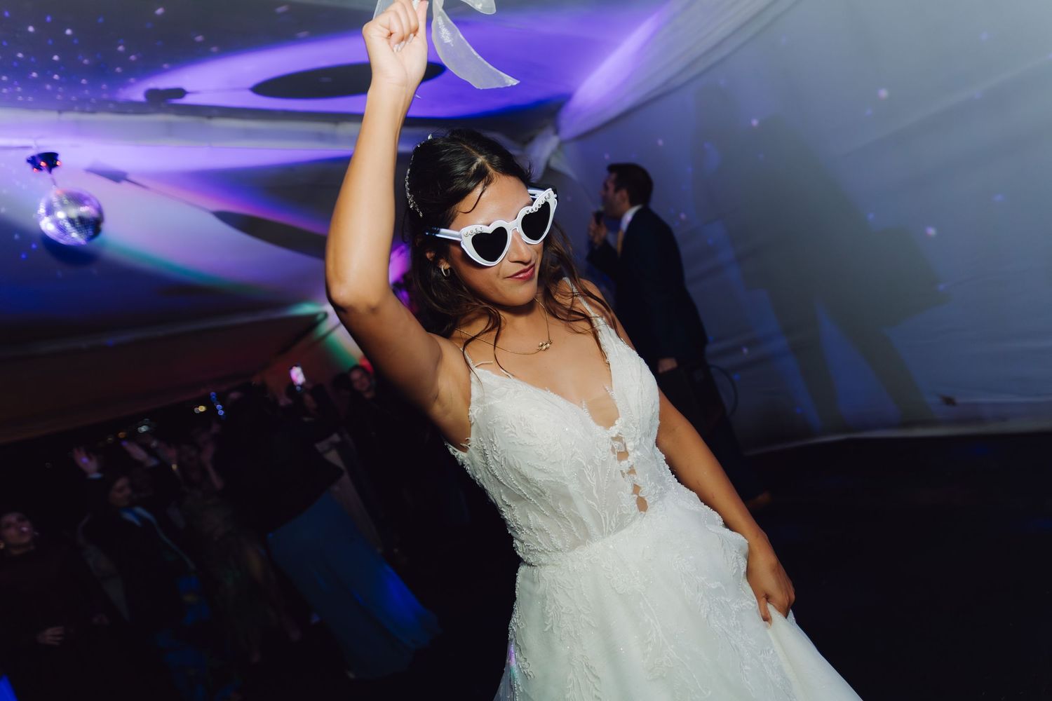 Joyful bride dances wearing heart-shaped sunglasses at wedding reception party.