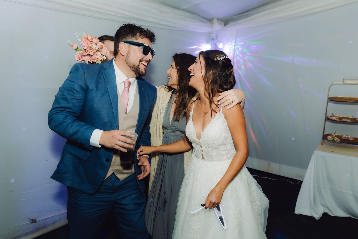 Bride and groom dancing with a guest at a wedding reception under disco lights.