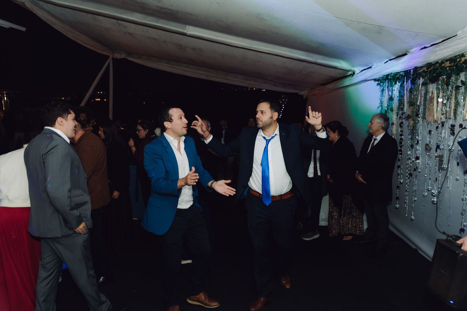 Male wedding guests dancing and celebrating at an outdoor evening wedding reception.