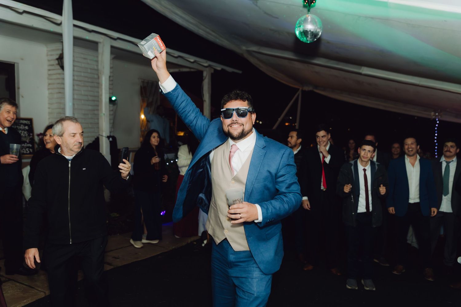 Groom in blue suit with sunglasses celebrating on the dance floor at his wedding.