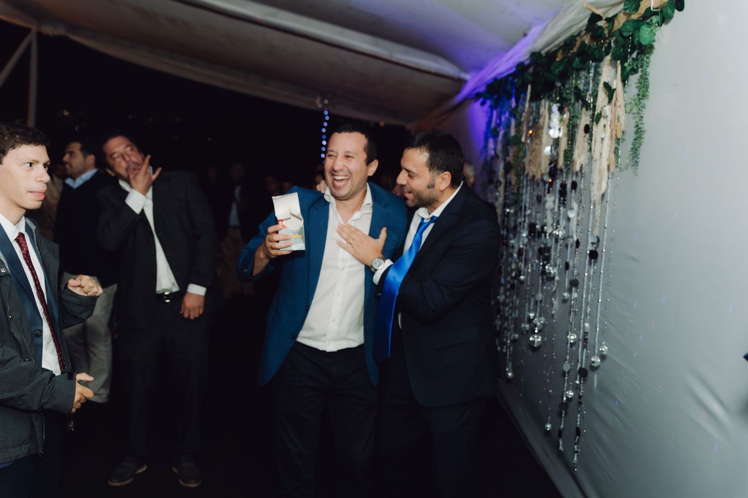 Two male wedding guests laughing and celebrating together at an evening wedding reception.