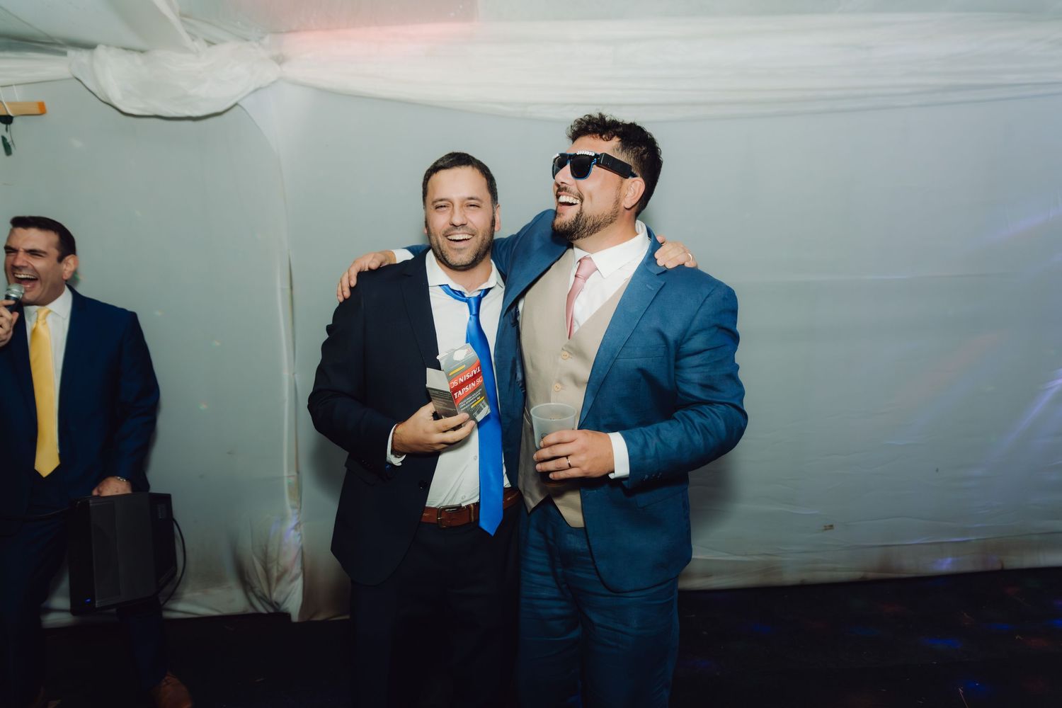 Two male wedding guests posing together with drinks at a wedding reception party.