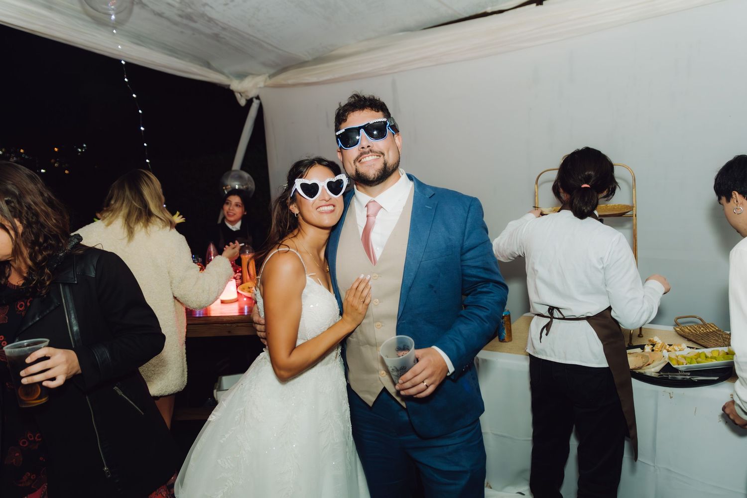 Bride and groom wearing novelty sunglasses posing together at their wedding reception.