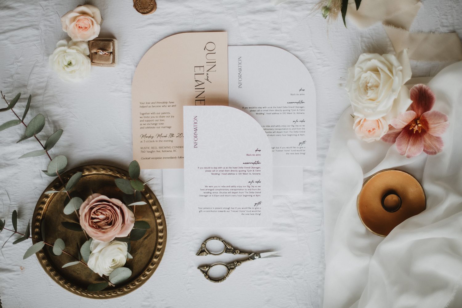 Elegant wedding invitation suite with blush roses, scissors, and gold accents on a white linen backdrop.