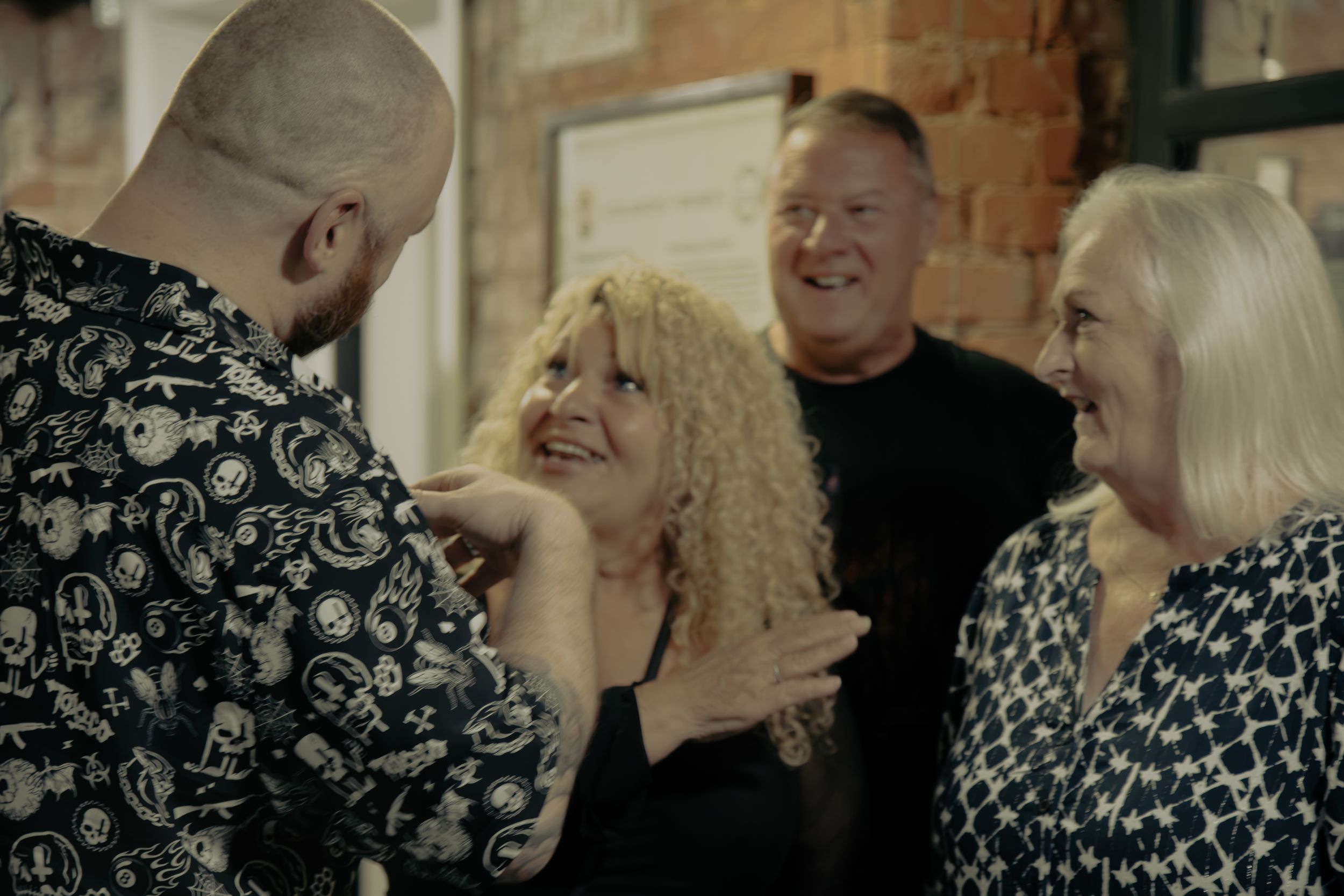 Group of adults laughing and socializing together in a warmly lit brick-walled venue at a social gathering.
