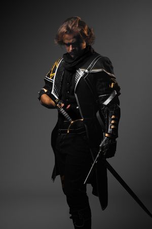A warrior in black and gold armor holds a sword, posing dramatically against a dark gray background.