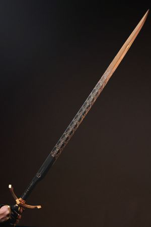Ornate fantasy sword with intricate engravings on blade, gold crossguard, held against dark background.