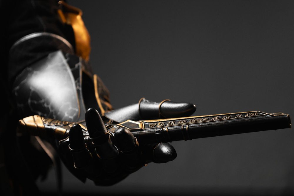Armored gauntlet holding an ornate antique flintlock pistol with gold engravings on dark background.