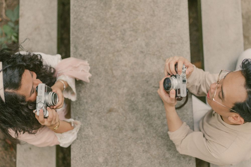 Two photographers photographing each other with vintage film cameras, captured from above on a wooden surface.