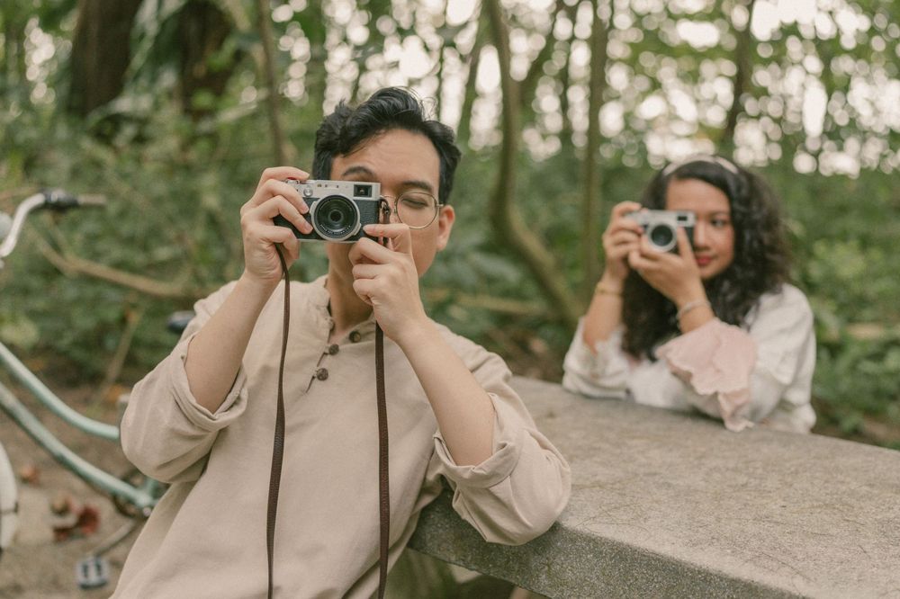 Two people photographing with vintage film cameras outdoors in a lush green park setting.