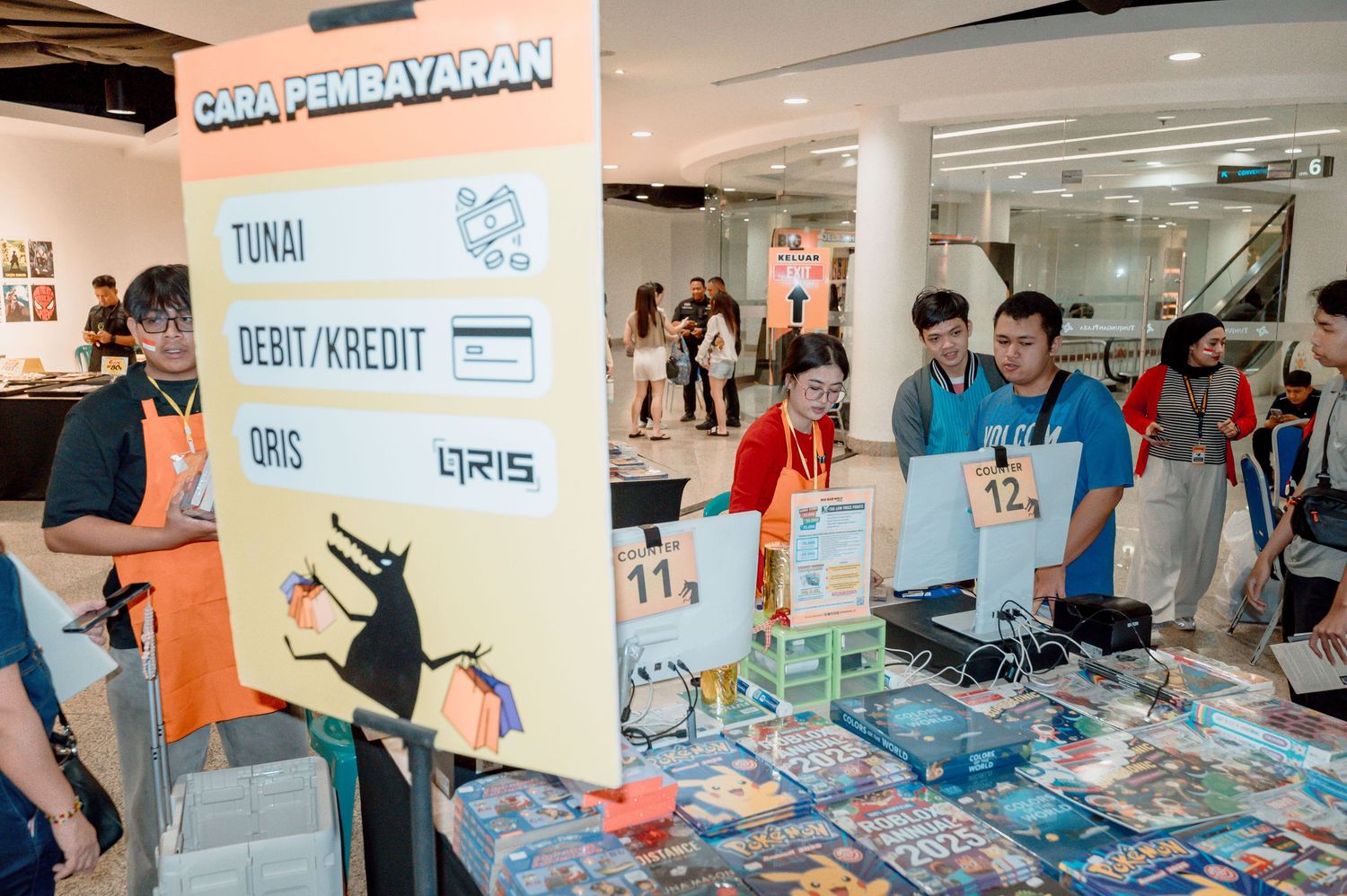 Event booth displaying payment methods including cash, debit/credit, and QRIS in a busy Indonesian shopping mall.